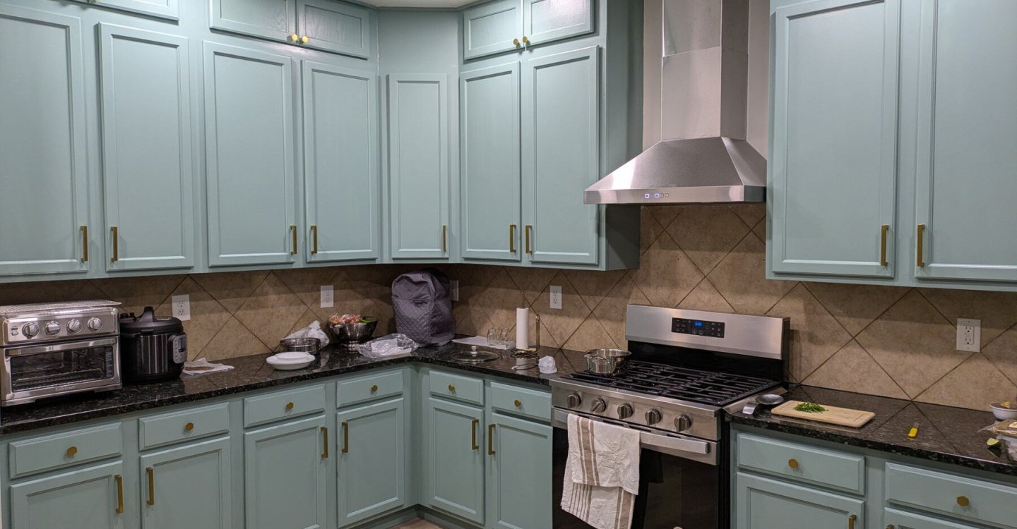 Kitchen with sage green cabinets, stainless steel range hood, gas range and dark granite worktops