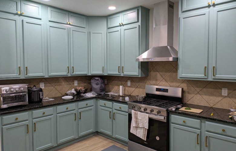 Kitchen with sage green cabinets, stainless steel range hood, gas range and dark granite worktops