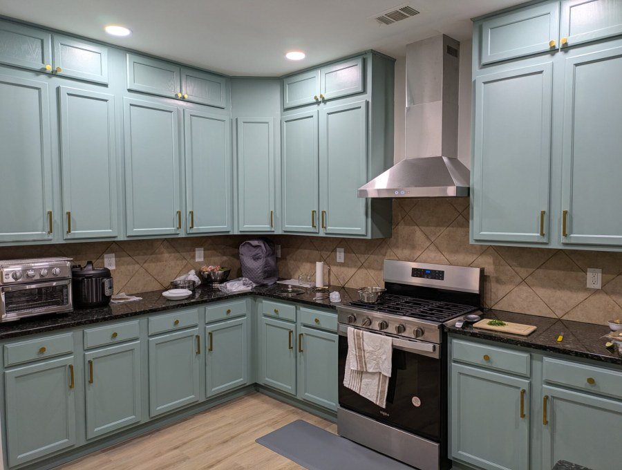 Kitchen with sage green cabinets, stainless steel range hood, gas range and dark granite worktops