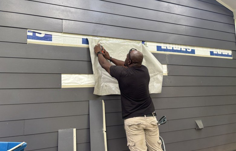 Carpenter fitting a length of grey horizontal siding to an exterior wall
